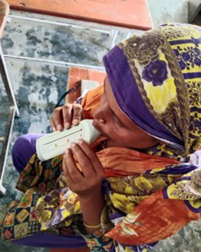 A child wearing a colorful headscarf drinks from a white bottle in a classroom setting.