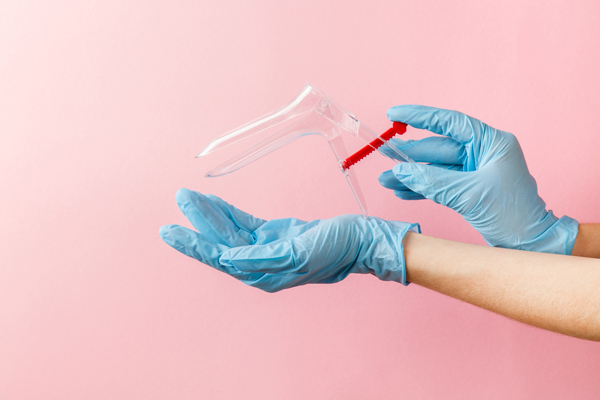 Hands in blue latex gloves holding a clear spray bottle with a red trigger, set against a pink background. Perfect for cleaning and disinfecting tasks.